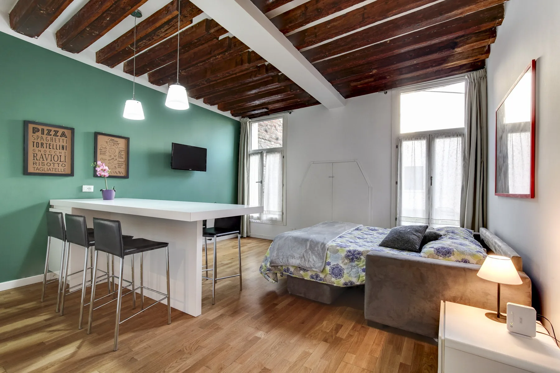 A bedroom with a bed beside a dining counter and stools.