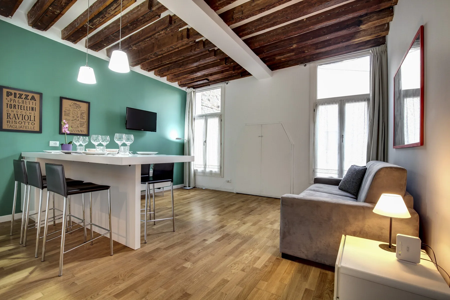 A bright living and dining area features a counter, seating, and exposed ceiling beams.