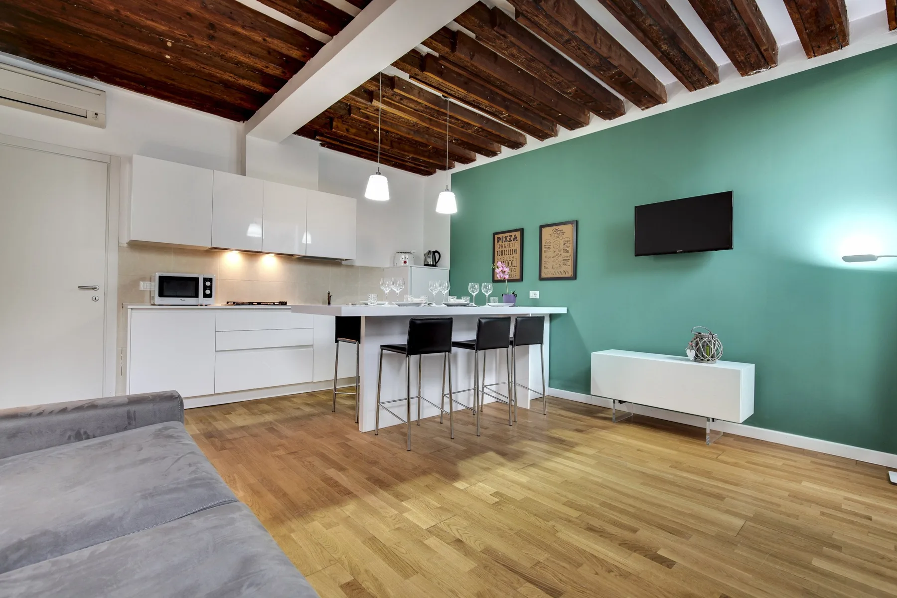 A kitchen and living area with a counter, seating, and exposed wooden ceiling beams.