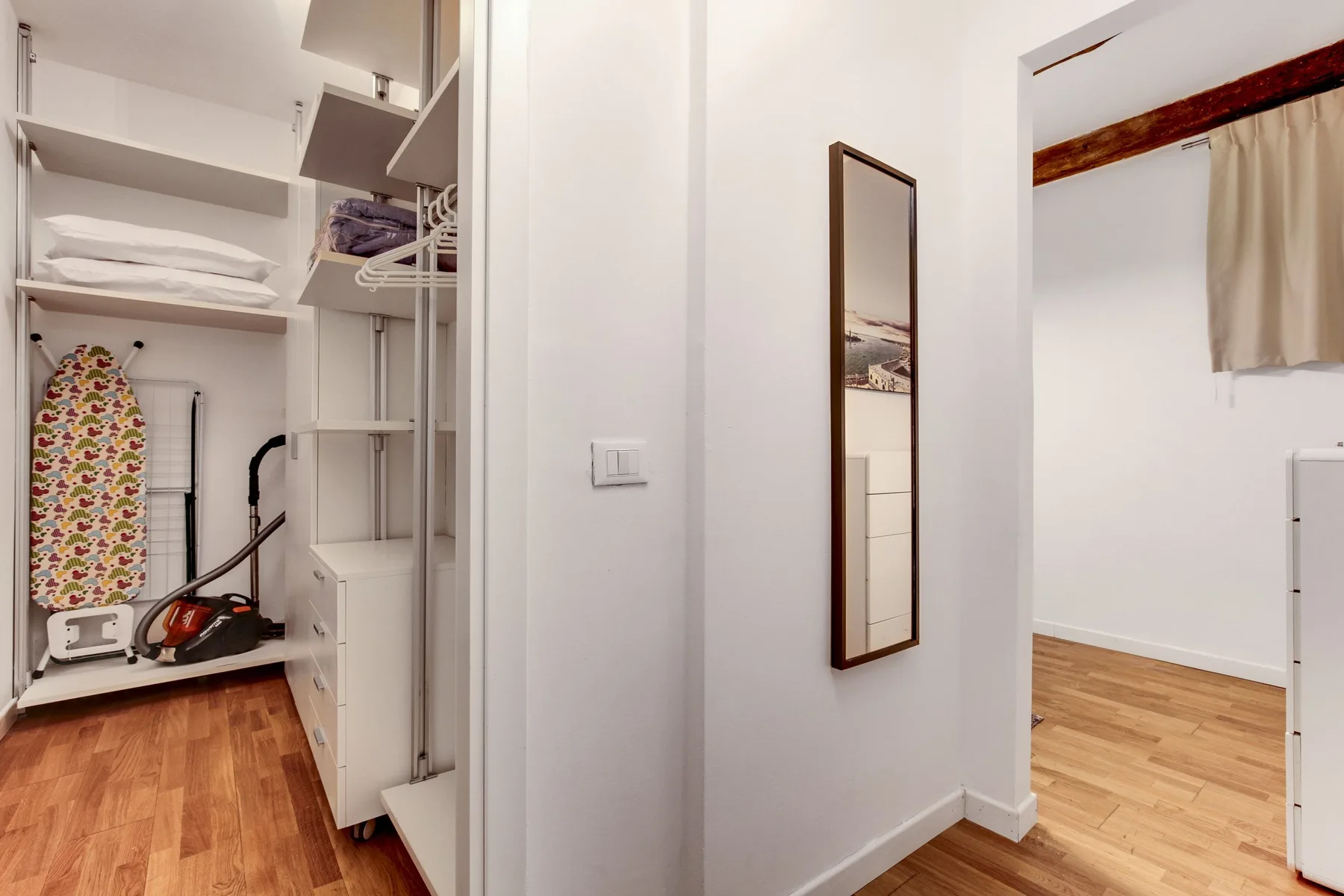 A bright hallway with an open storage closet and a doorway to a room.