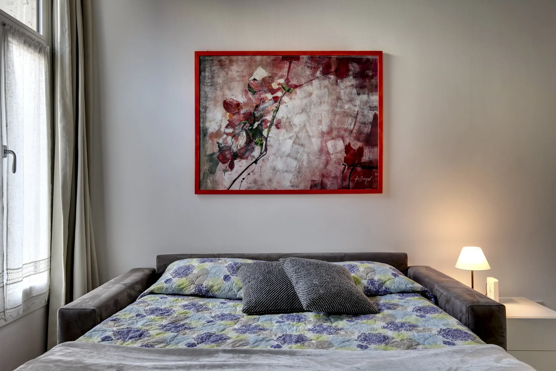 A bedroom with a bed beneath a framed floral painting.