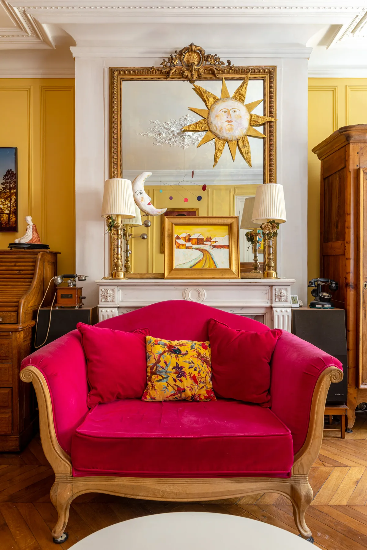 A bright pink seating area sits beneath a decorative sun artwork and ornate mirror.
