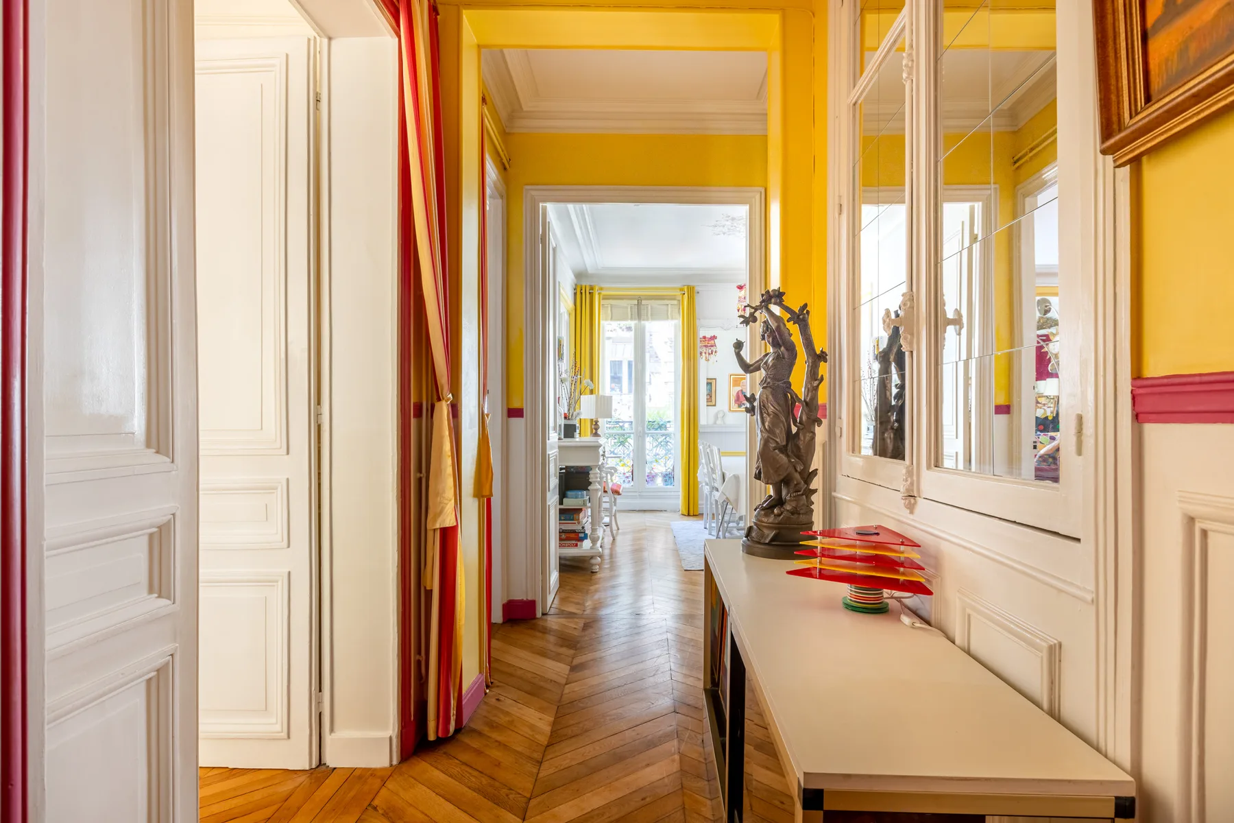 A bright hallway with yellow walls, mirrored panels, and a long console table.
