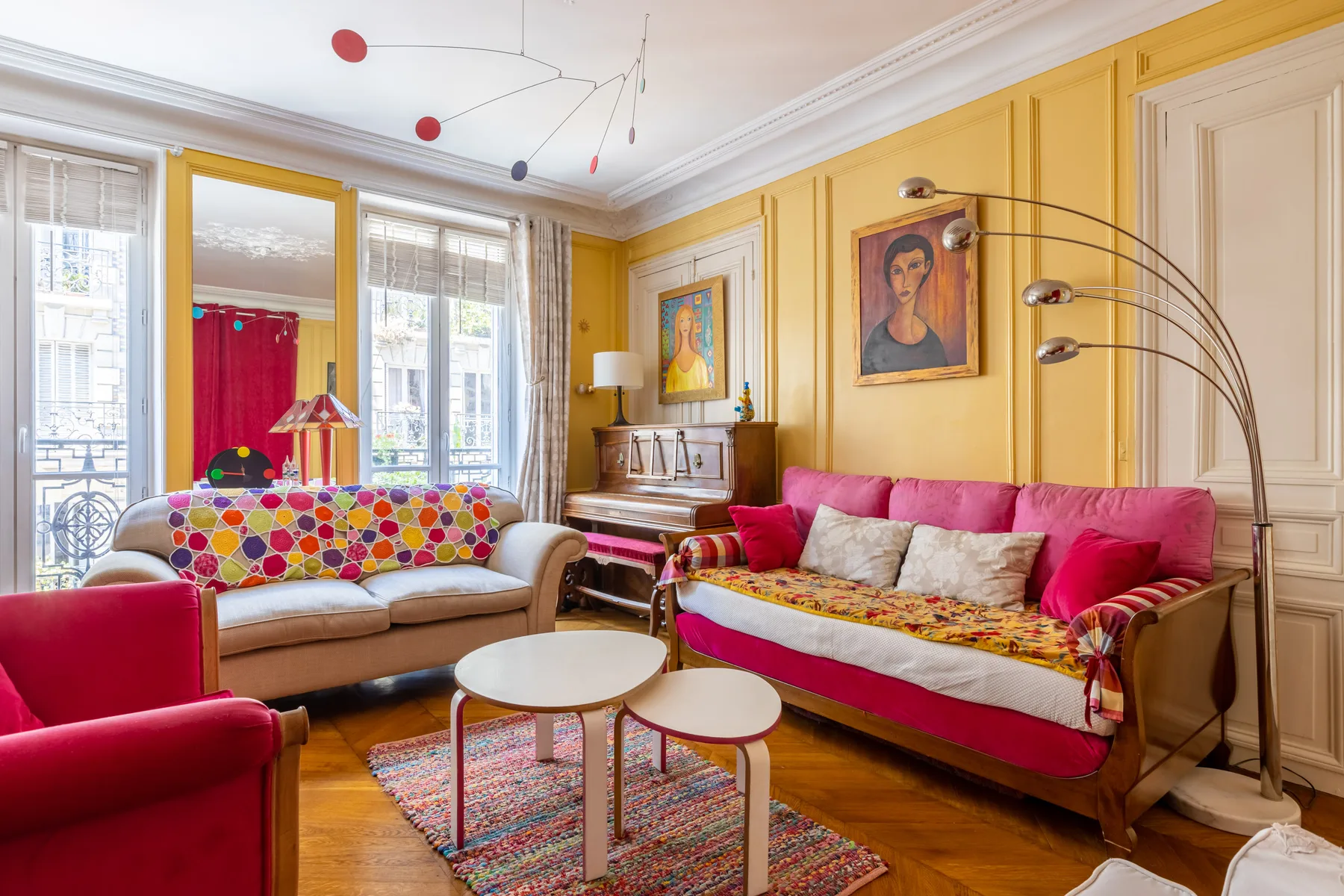 A colorful living room with red and beige seating and tall windows.