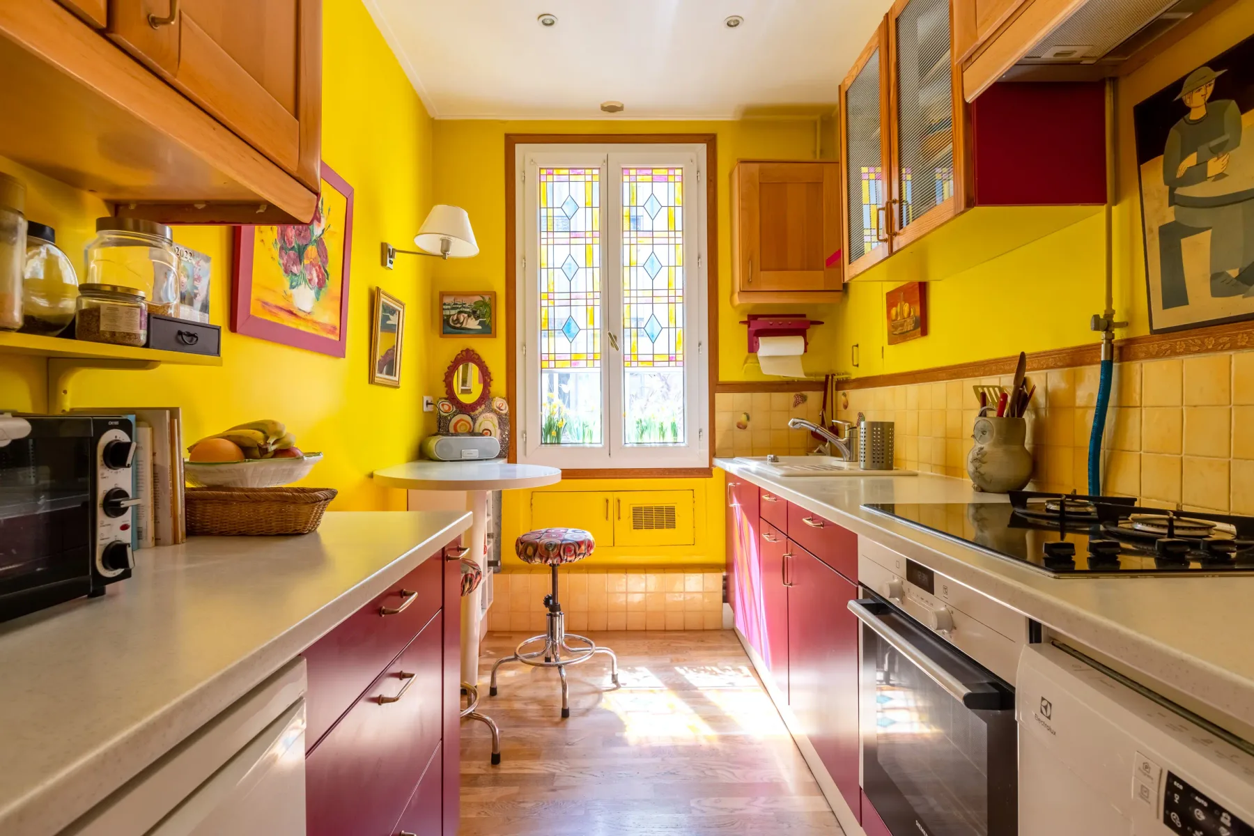 Una cocina luminosa con paredes amarillas, gabinetes rojos y una ventana.