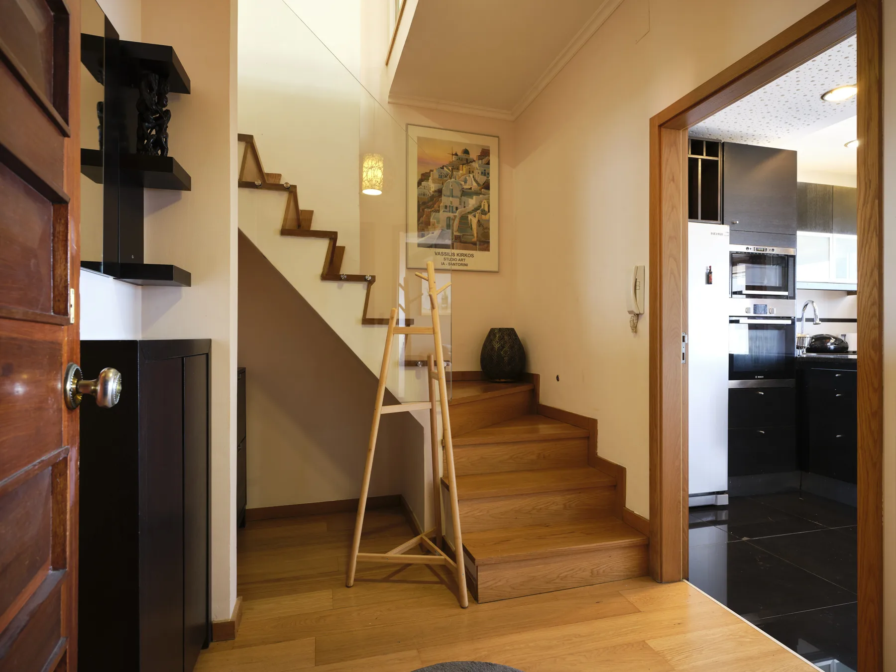 A wooden staircase rises beside a small entry area, with the kitchen visible through a doorway.