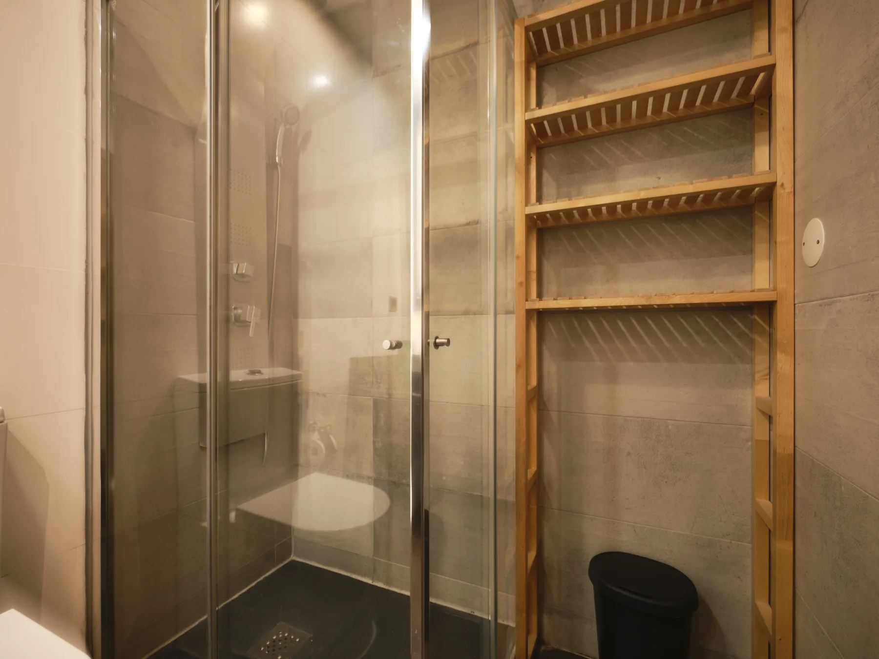 A bathroom with a glass shower and wooden shelving.