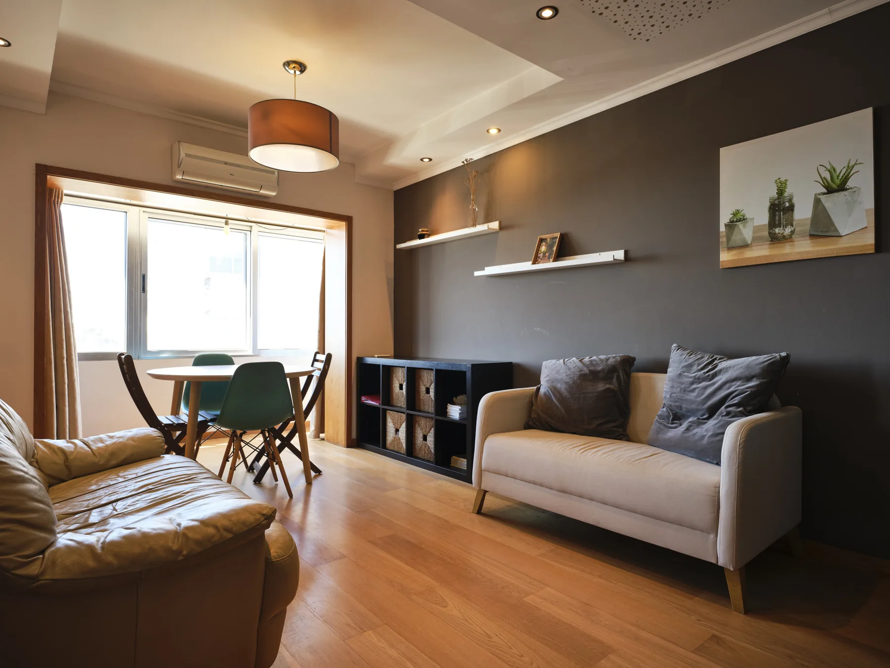 A living room with seating, shelving, and a dining table beside the window.