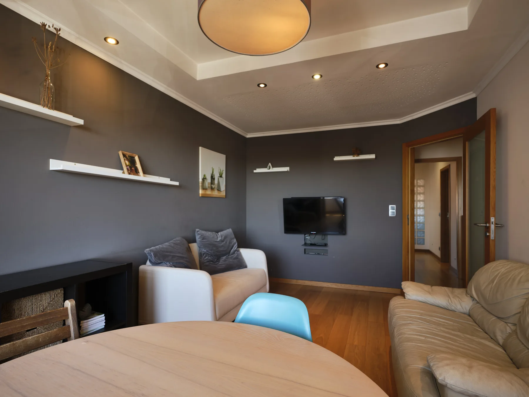 A living room with seating, a wall-mounted television, and a round table.