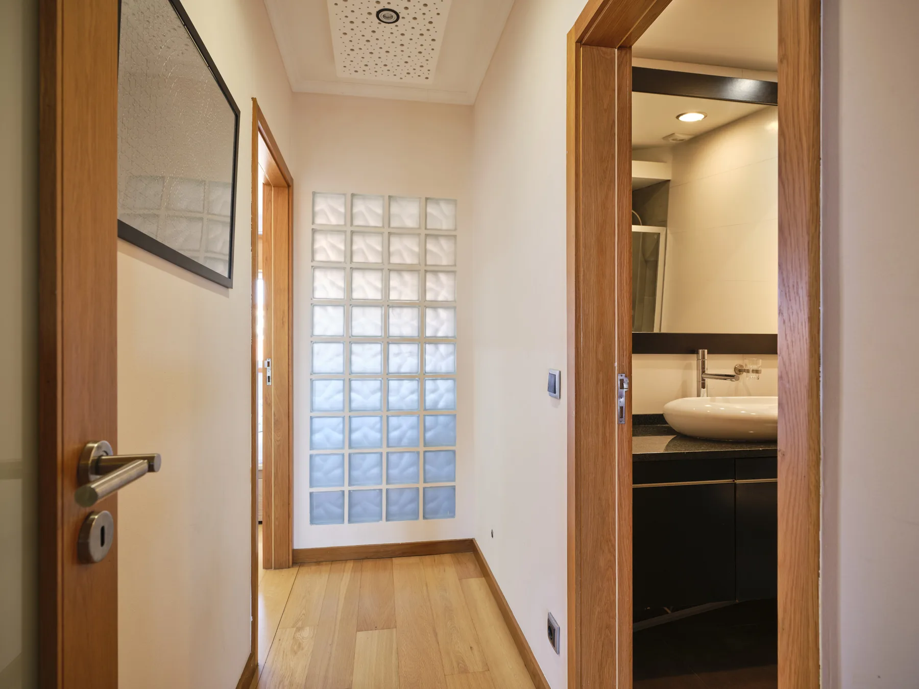 A hallway with a glass-block window and an open bathroom doorway.