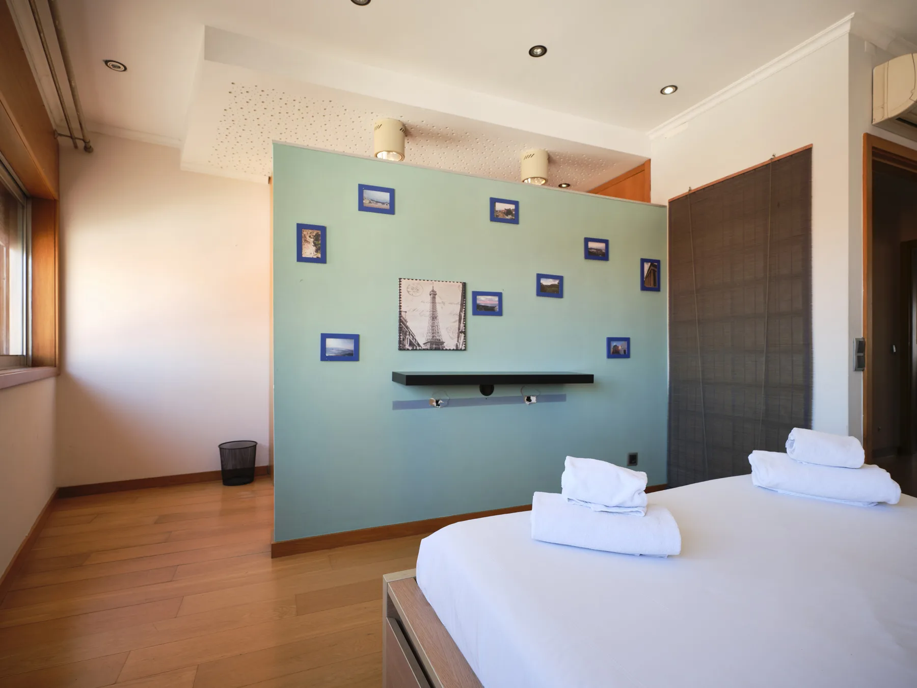 A bedroom with a bed, white linens, and a teal wall decorated with framed pictures.