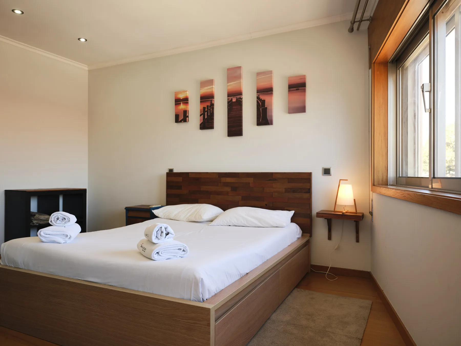 A bedroom with a bed, bedside table, and large window.