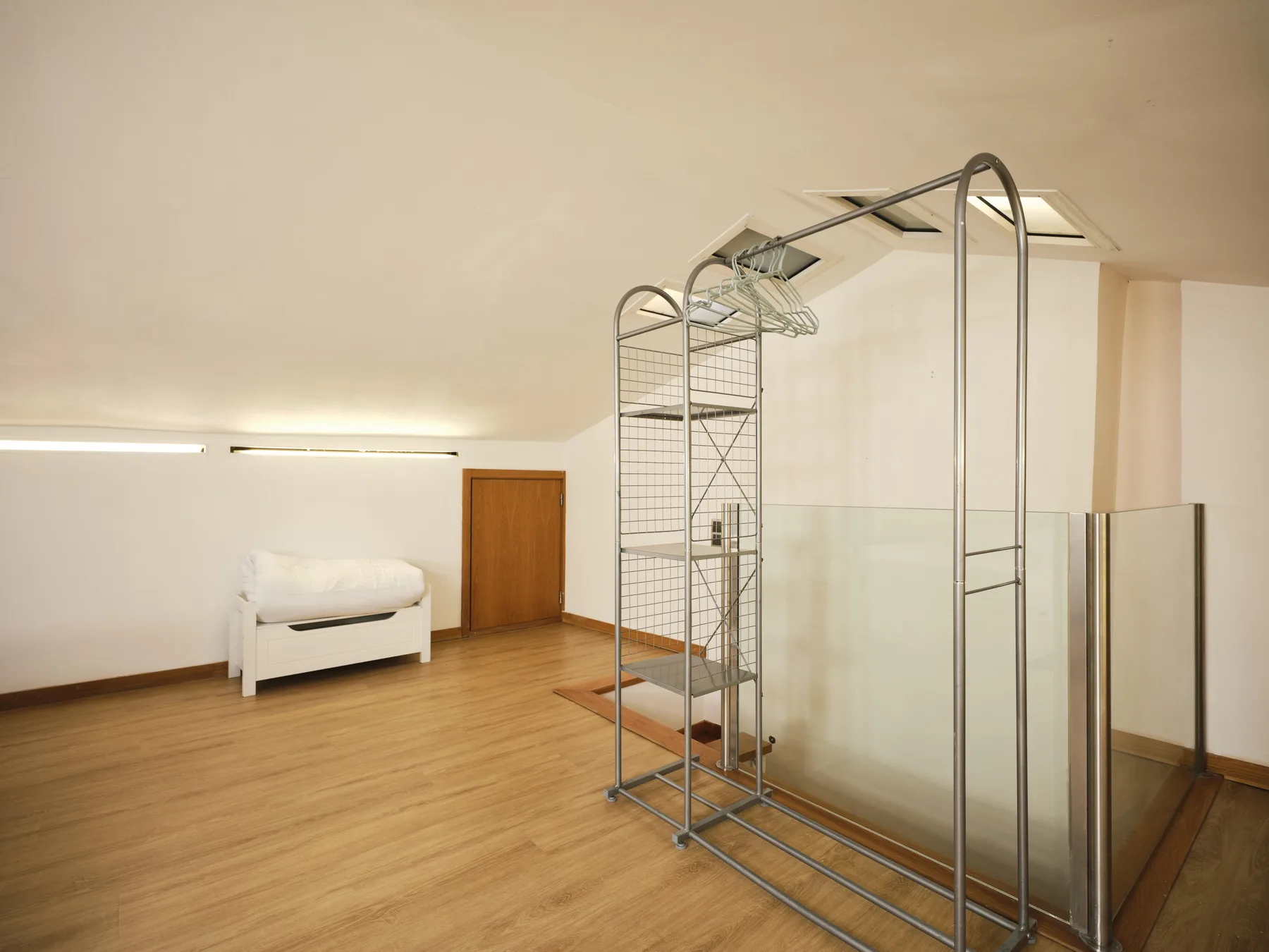 A spacious room with wood flooring, a low bed, and a metal clothing rack.