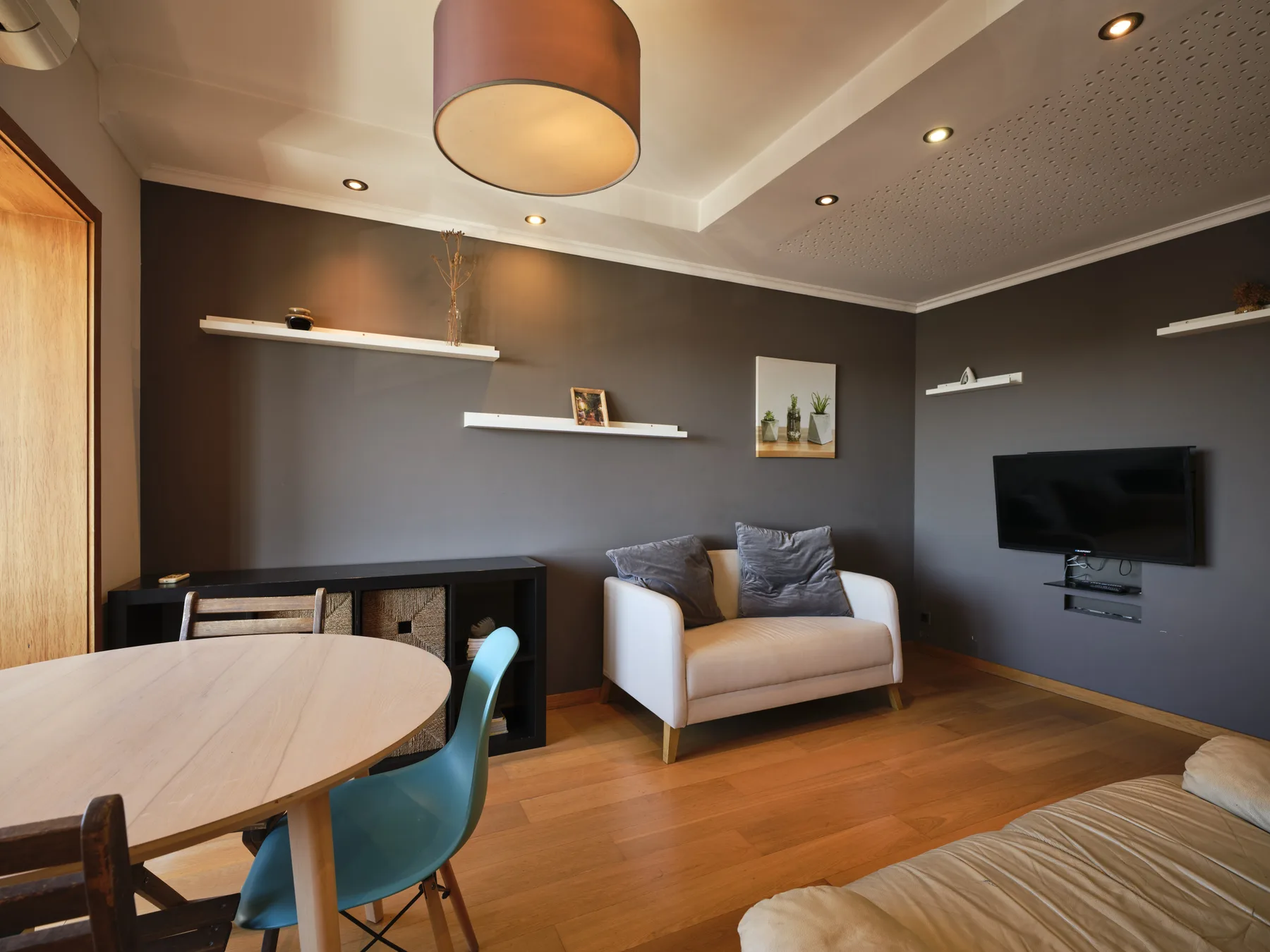 A living area with seating, a wall-mounted television, and a dining table.