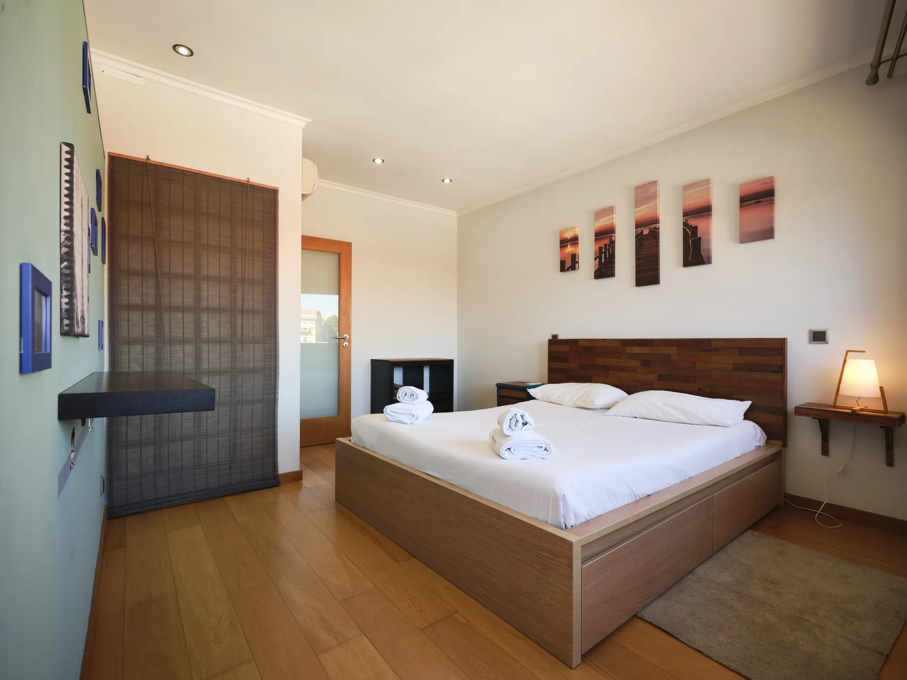 A bedroom with a large bed, wall art, and a small bedside table.