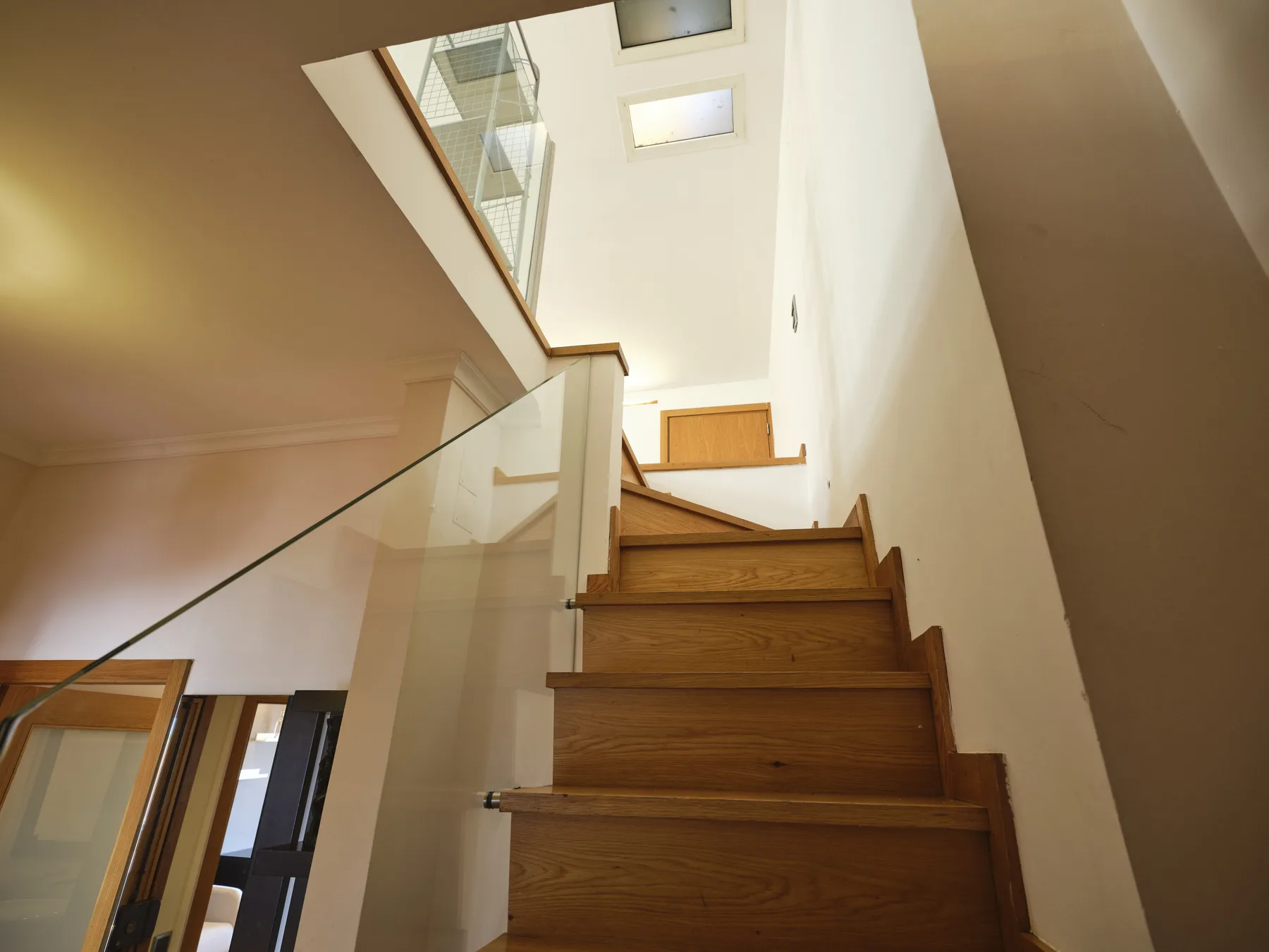 A wooden staircase with a glass railing leads up through a bright interior.