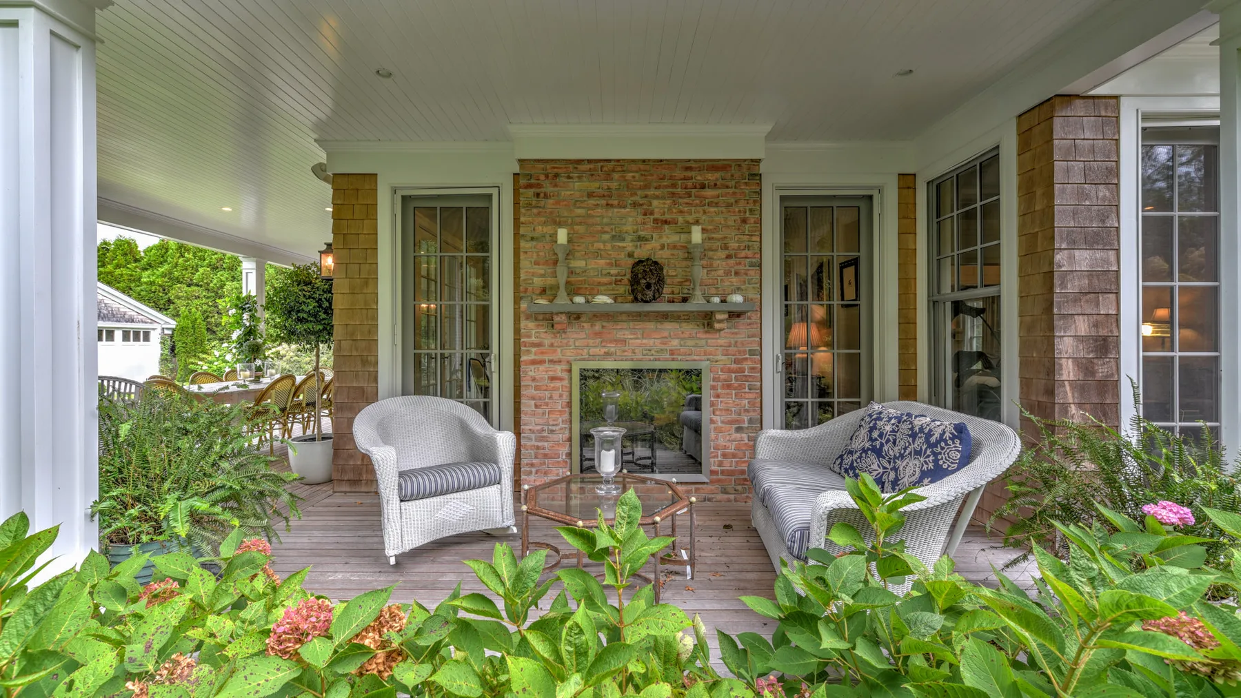 Un porche cubierto tiene asientos de mimbre, una chimenea de ladrillo y plantas.
