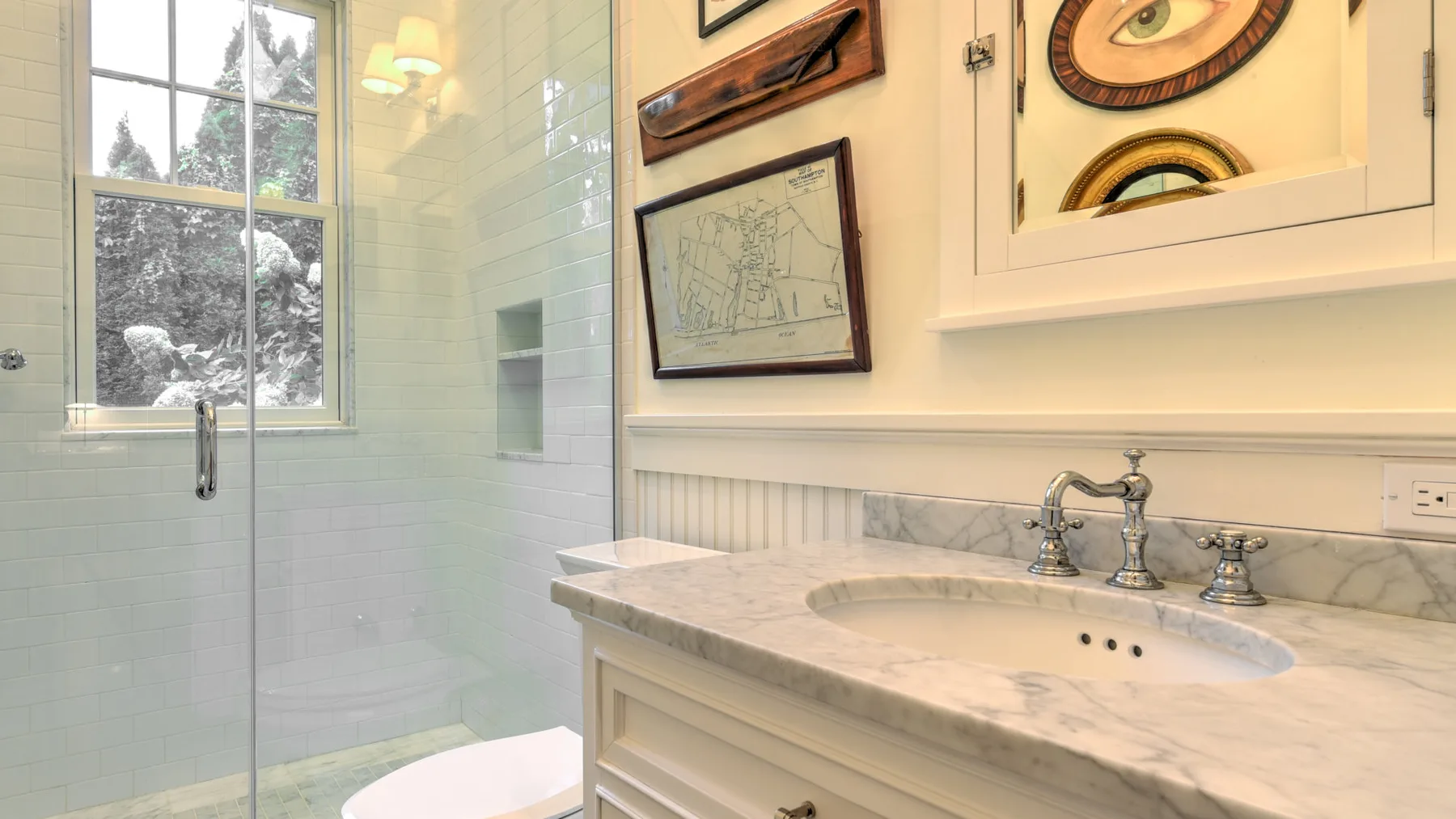 Un baño luminoso con un tocador de mármol y una ducha de vidrio.
