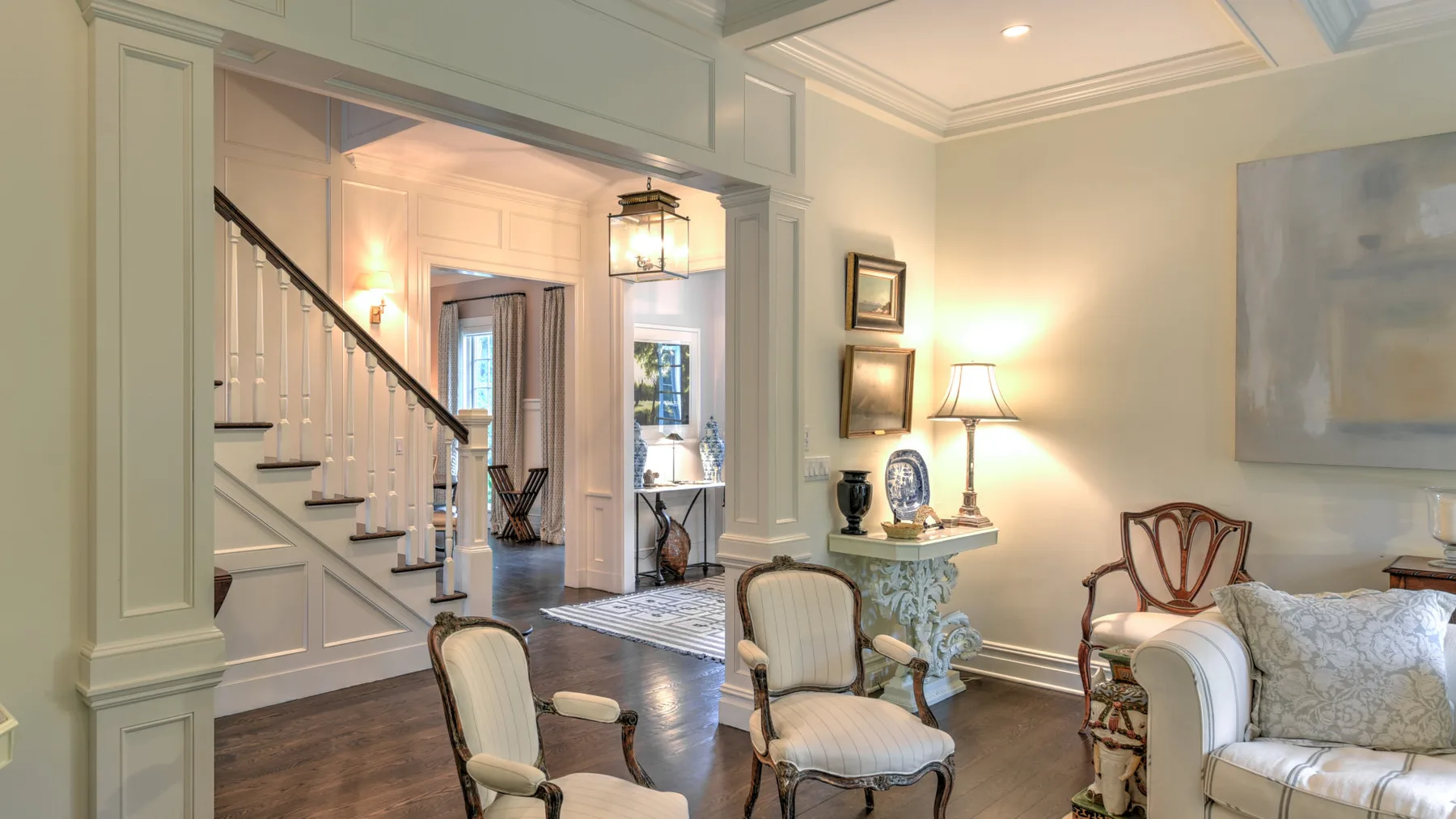 Una luminosa sala de estar con una escalera, asientos y una pequeña mesa decorativa.