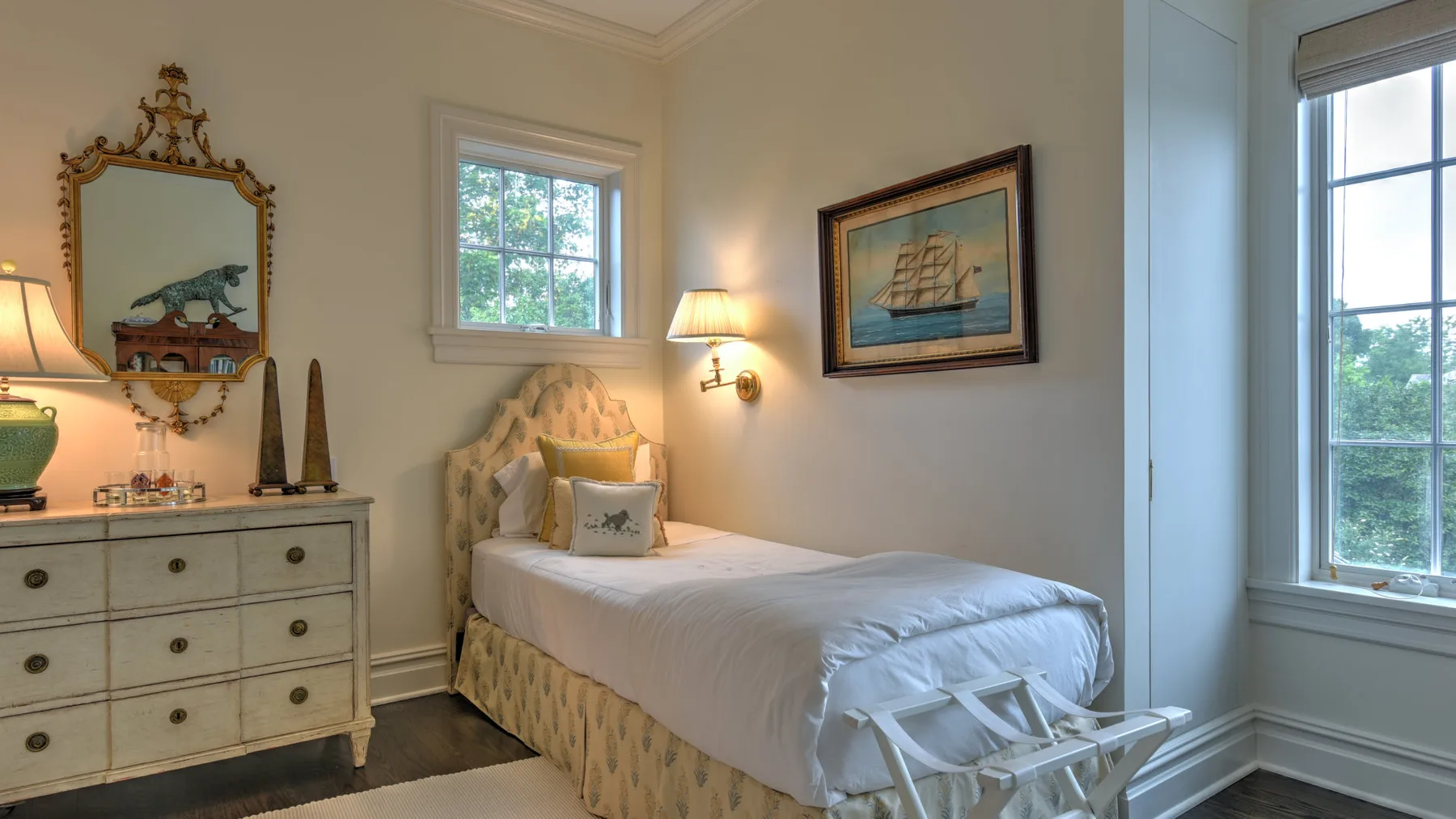 Un dormitorio con una cama junto a una cómoda y ventanas grandes.