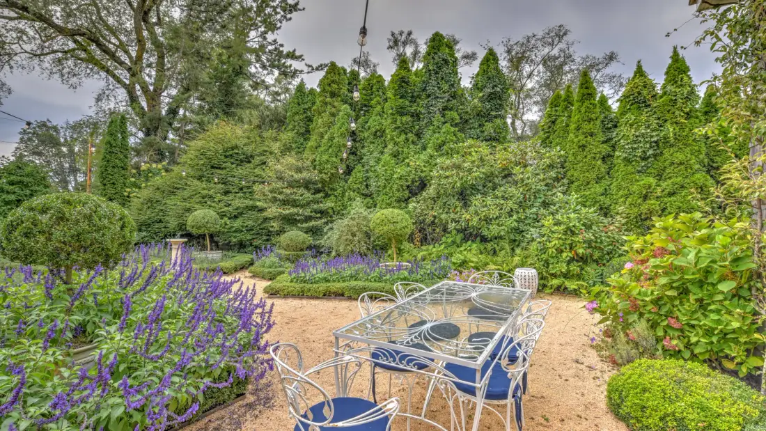 Un patio de jardín con asientos metálicos, una mesa y flores moradas.
