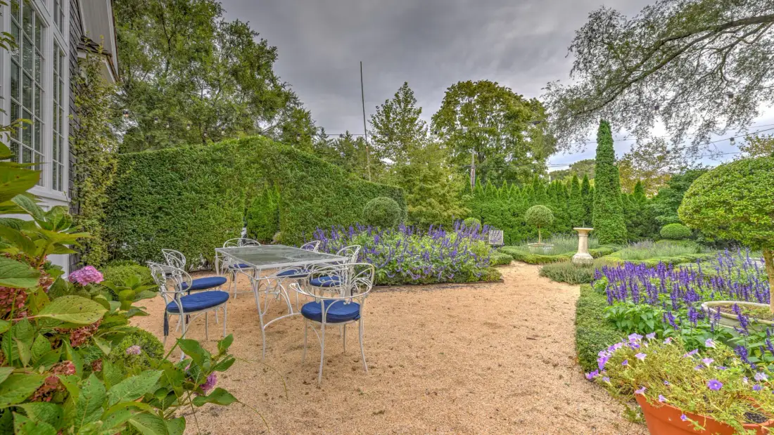 Un patio de jardín tiene asientos metálicos junto a parterres y setos recortados.