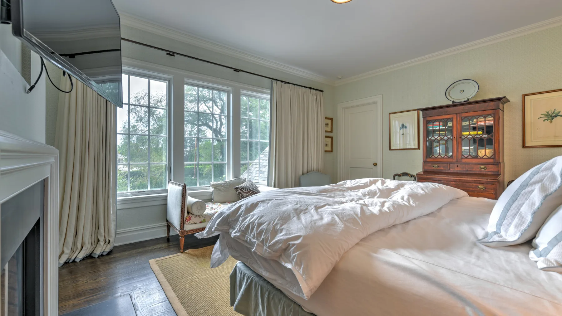 Un dormitorio luminoso con una cama grande junto a ventanas altas y cortinas.