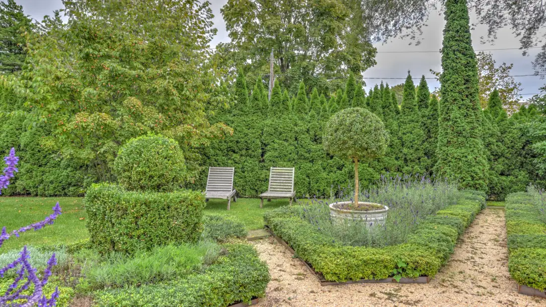Un jardín ajardinado con dos asientos exteriores junto a setos recortados.