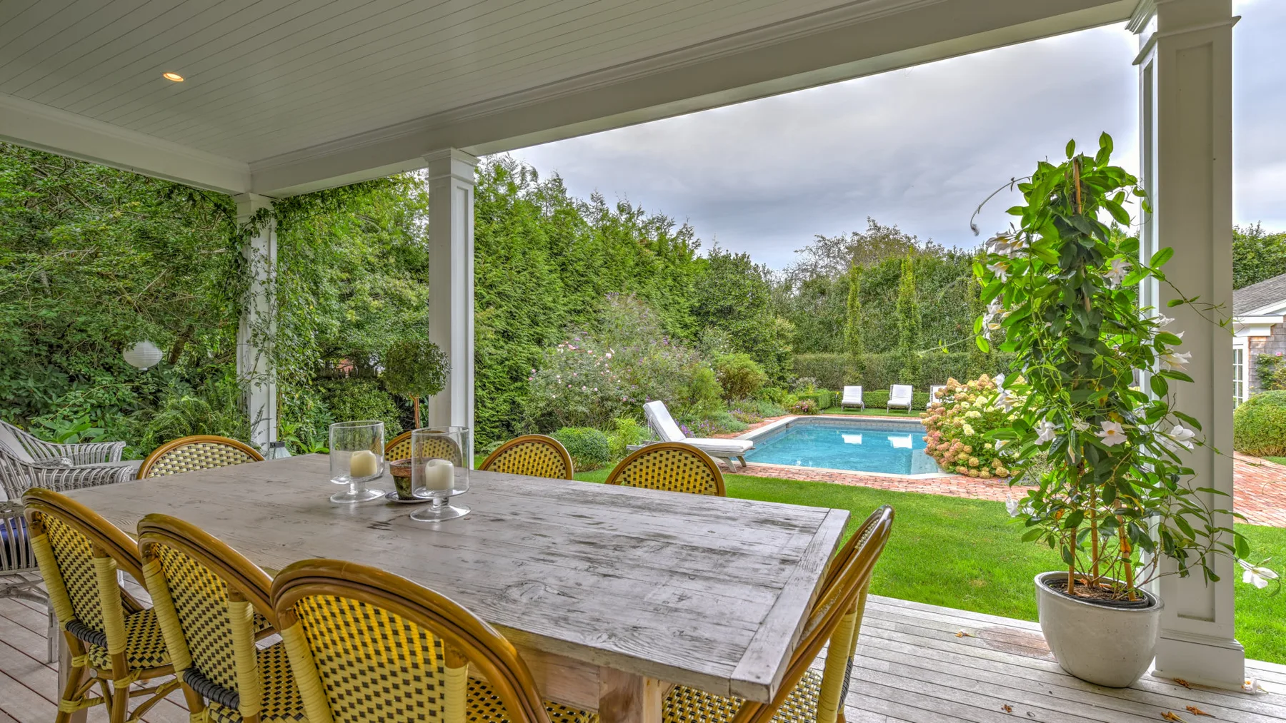Una zona de comedor exterior cubierta da a una piscina y un jardín.