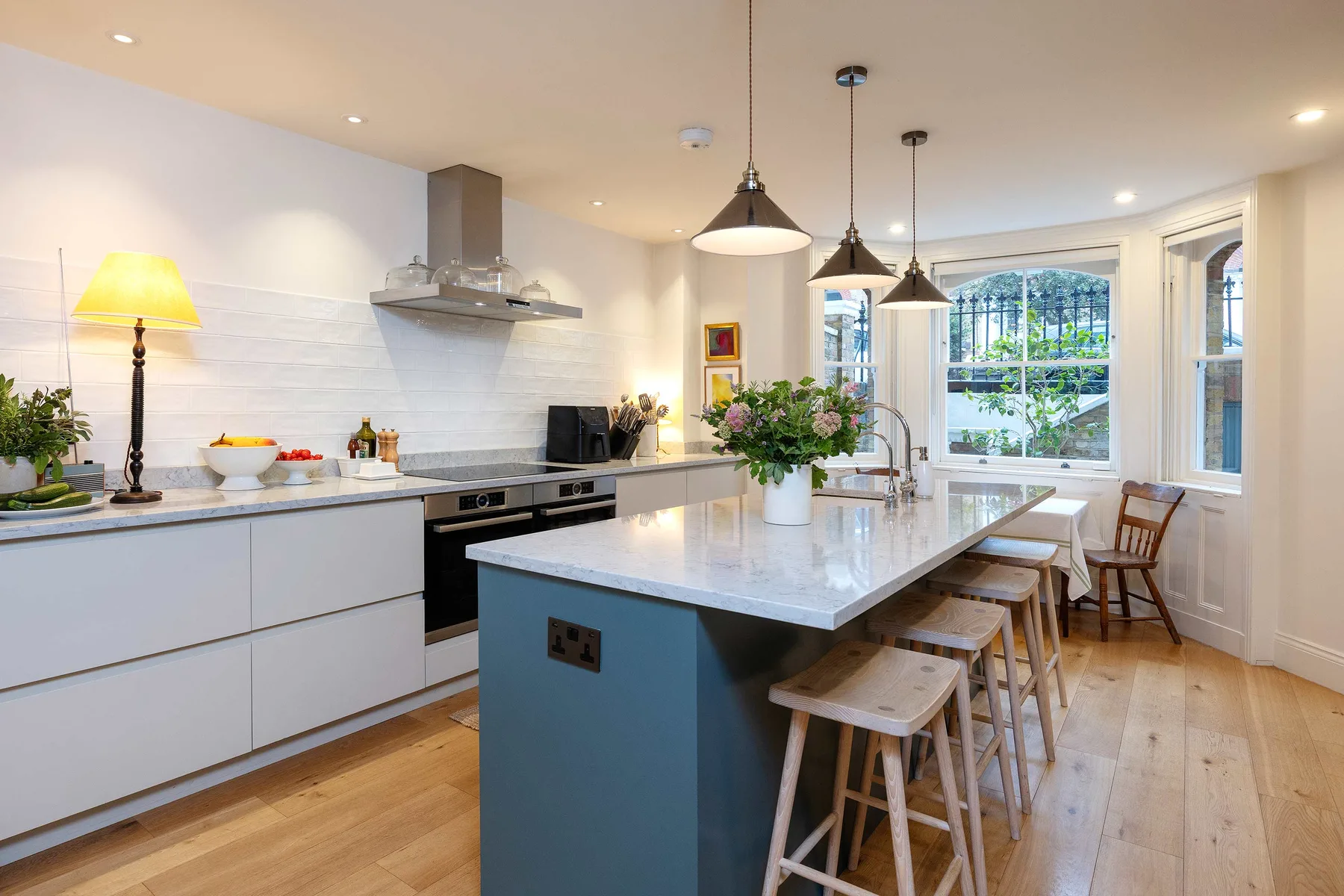 A bright kitchen with a large island, pendant lights, and windows overlooking greenery.