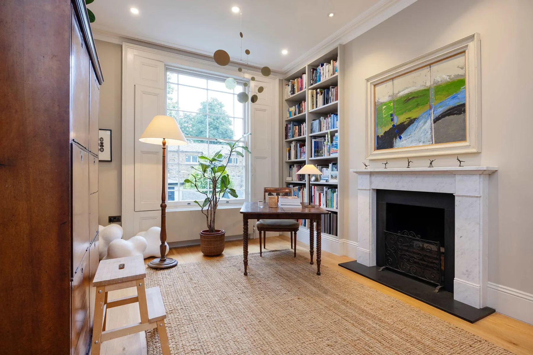 A bright living room with a fireplace, bookshelves, and a table by the window.