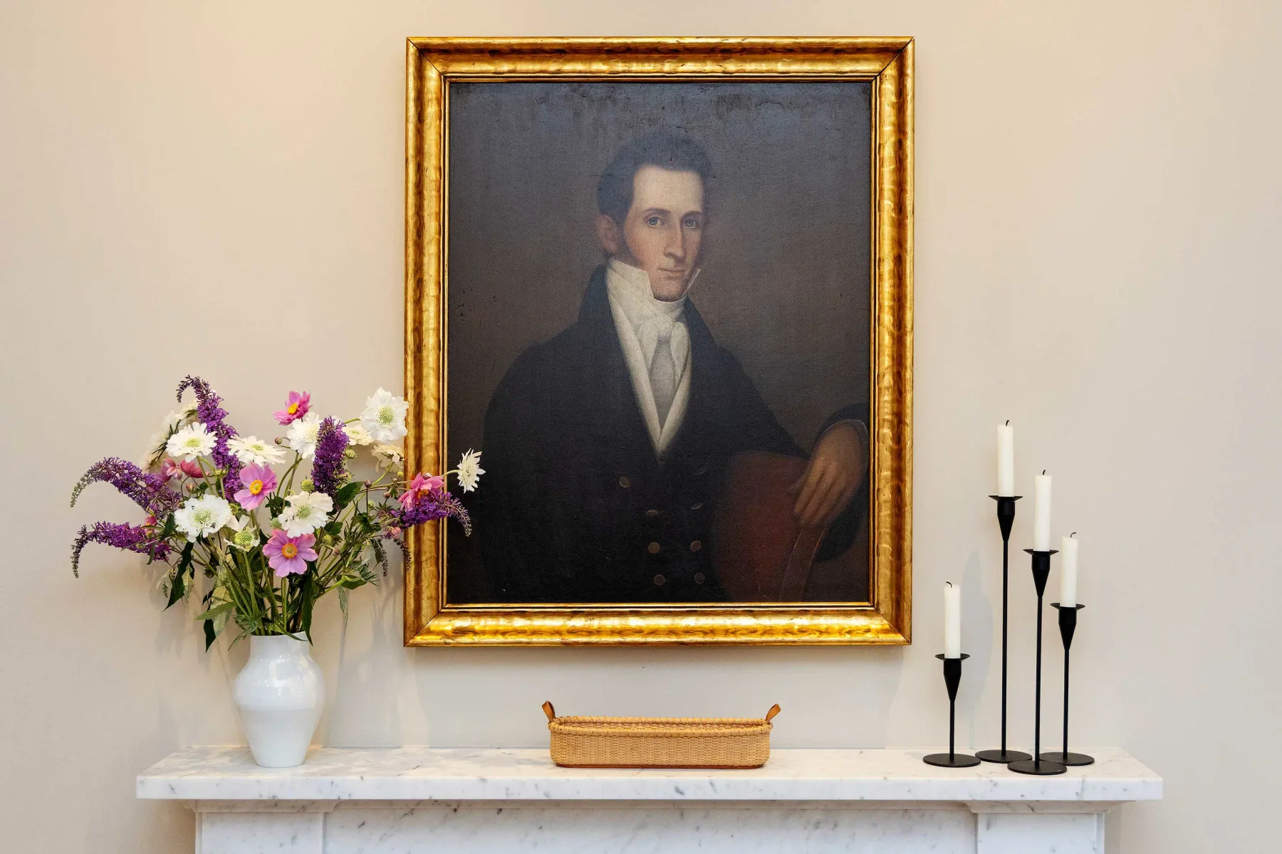 A framed portrait hangs above a mantel decorated with flowers and candles.