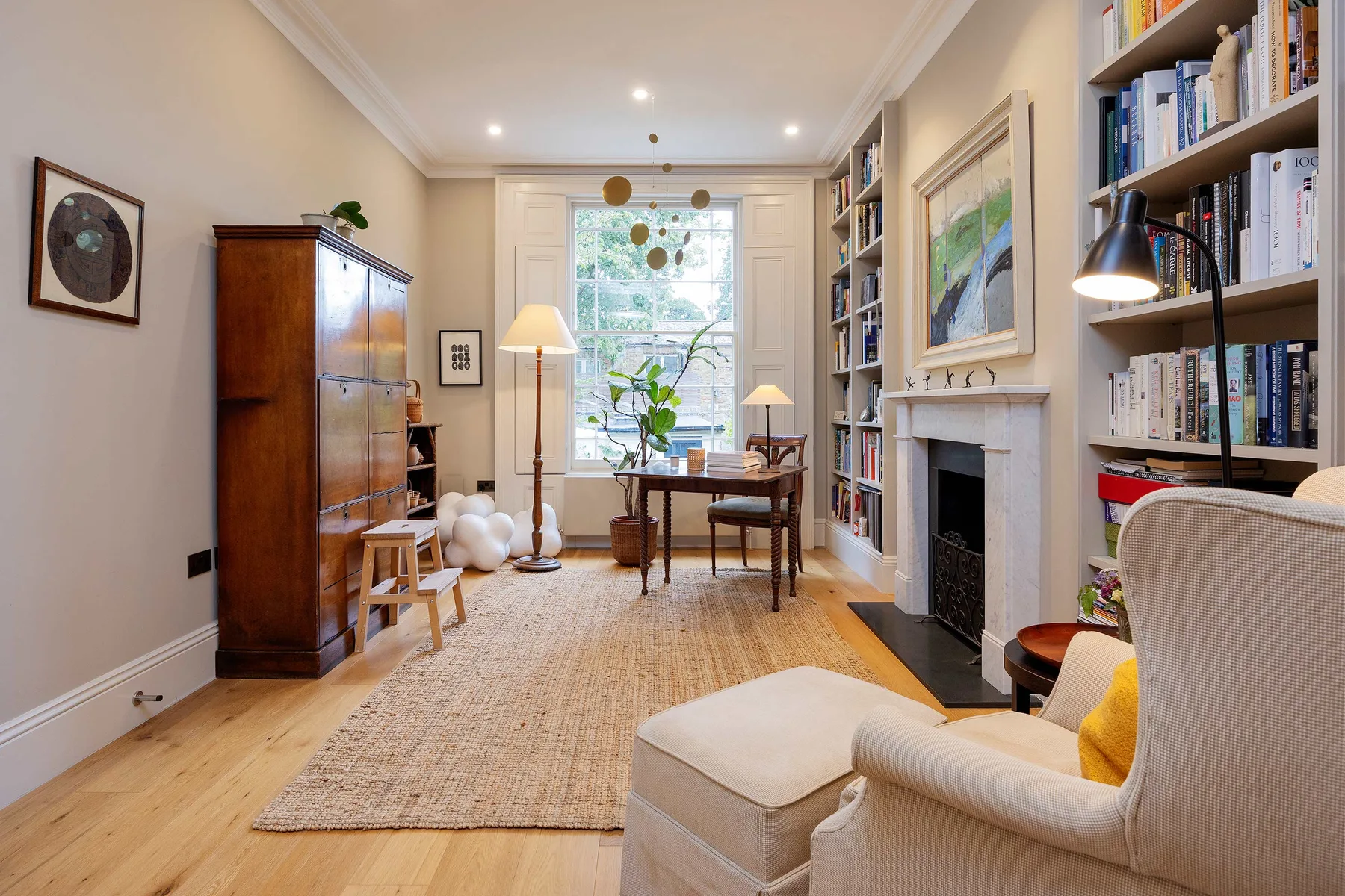 A bright living room with a book-lined wall and a table beside the window.
