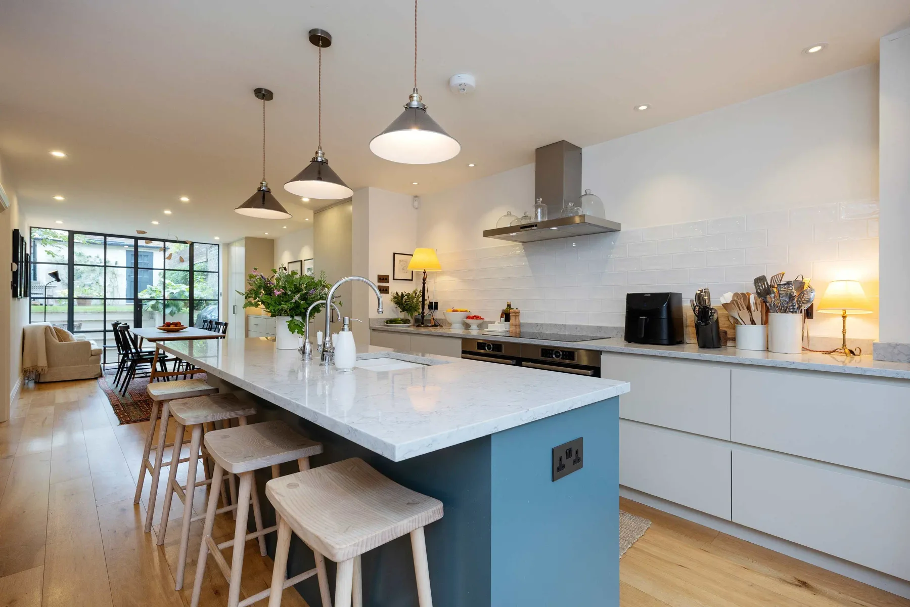 A bright kitchen with a large island and dining table beside tall windows.