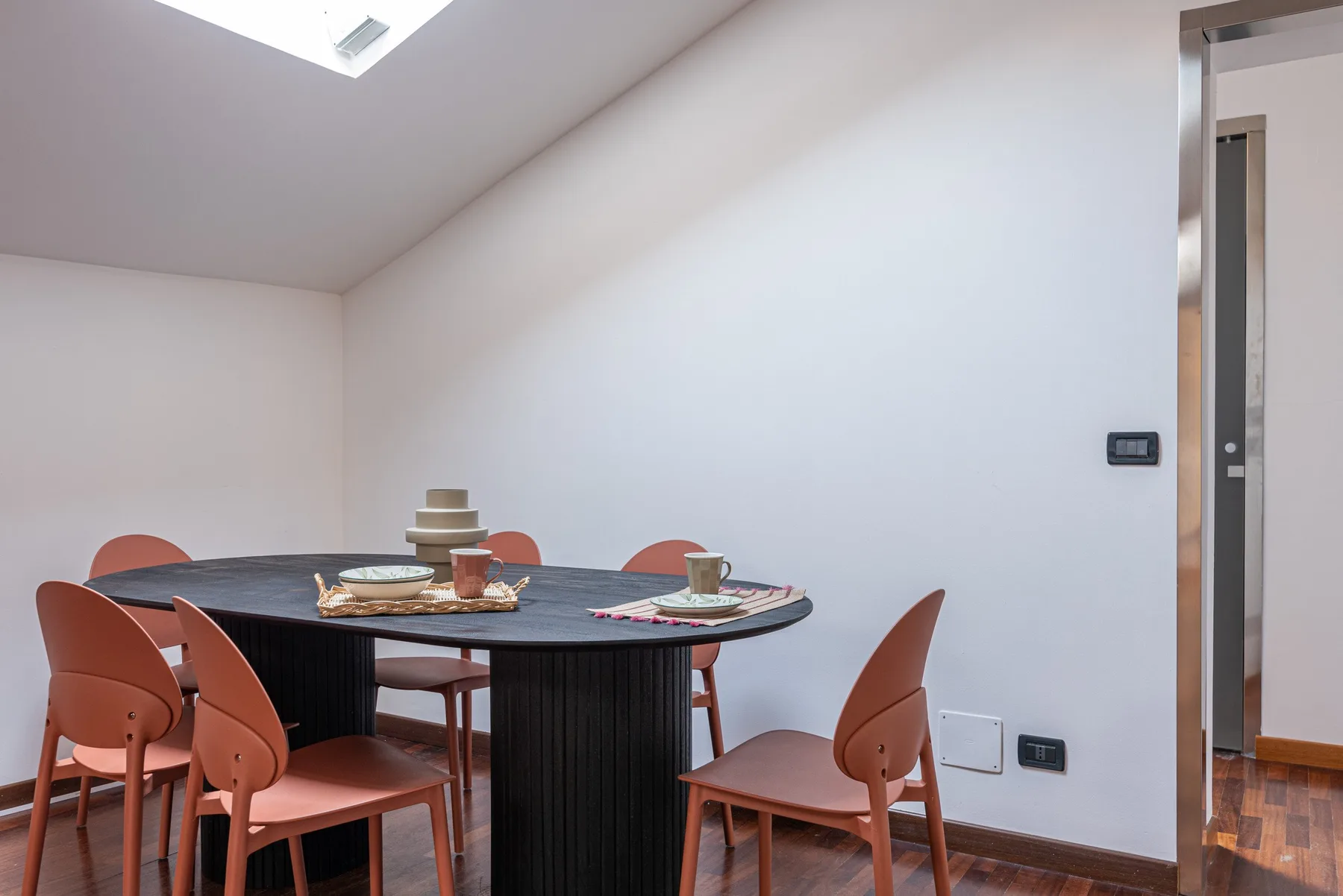 Un comedor con una mesa oscura y asientos de color terracota.