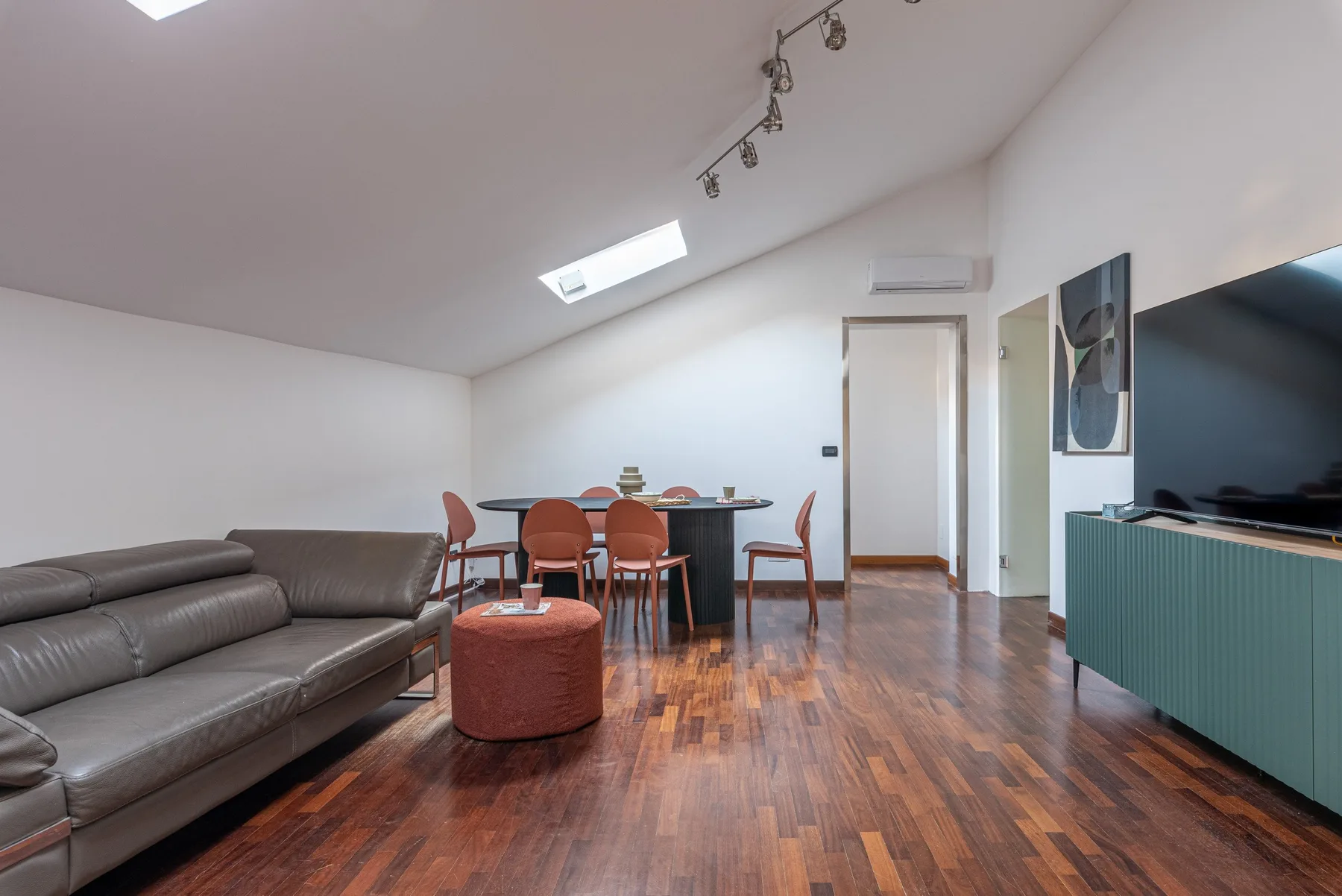 A modern living and dining area with seating, a table, and a television.