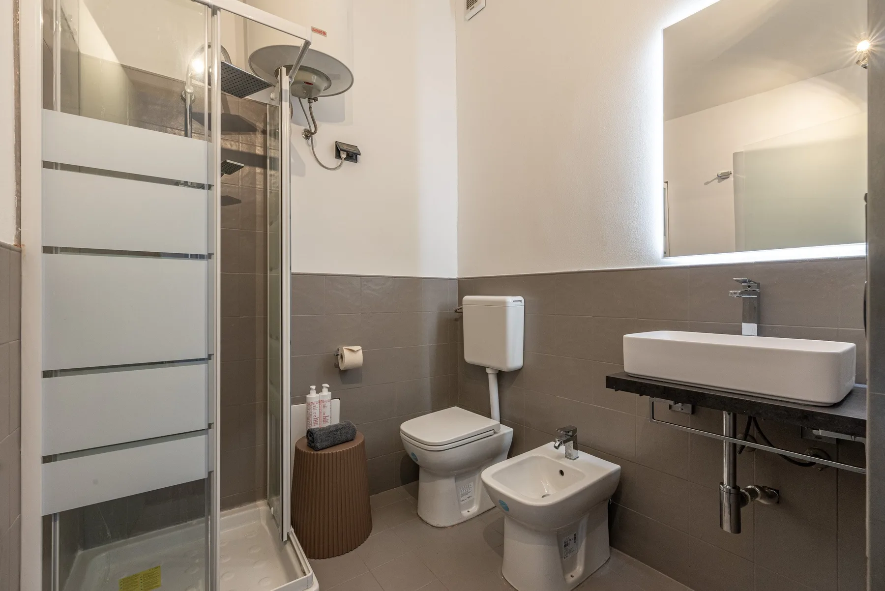 Un baño con ducha de vidrio, inodoro y lavabo bajo un espejo grande.