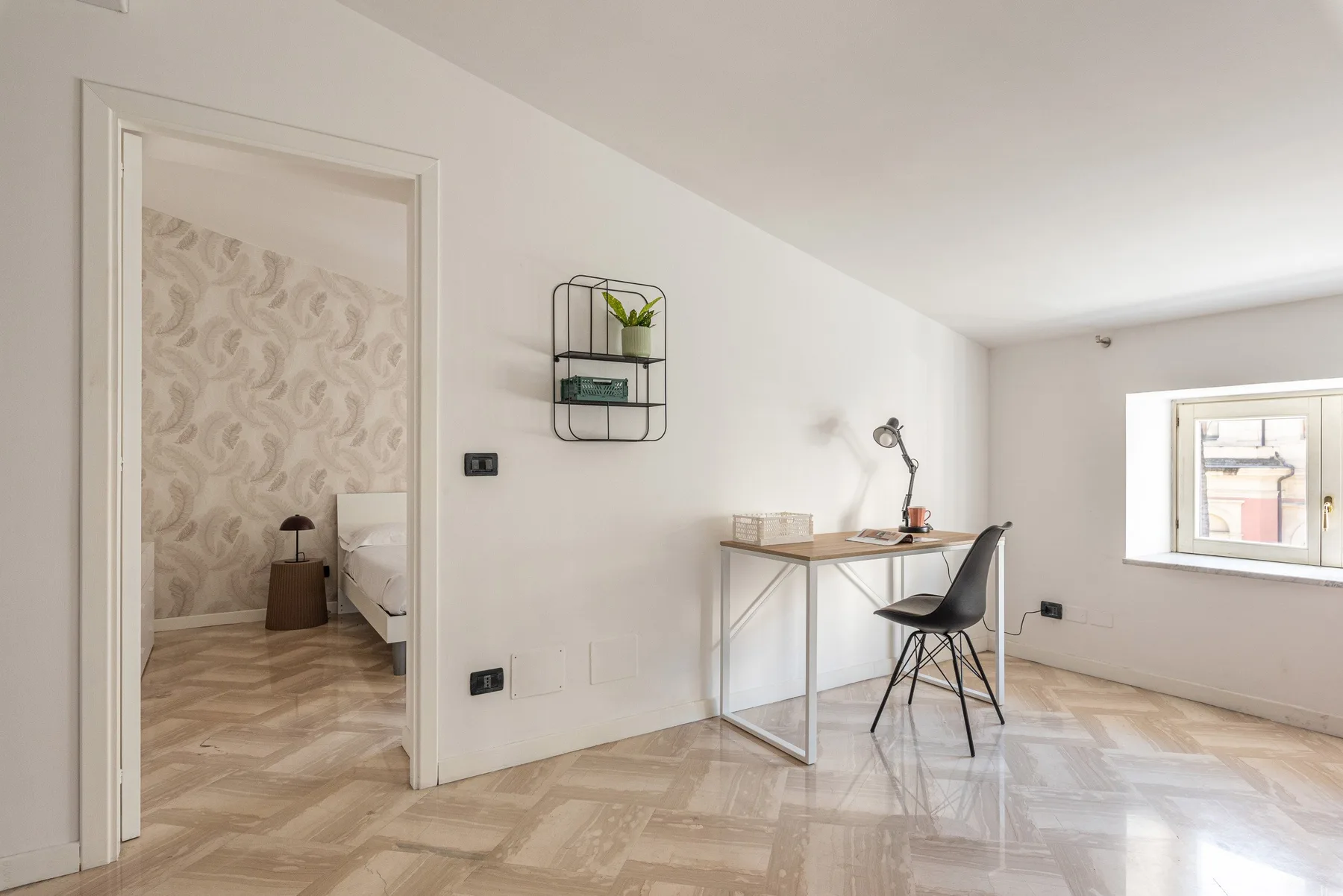 A bright room with a desk and chair beside an open doorway to a bedroom.