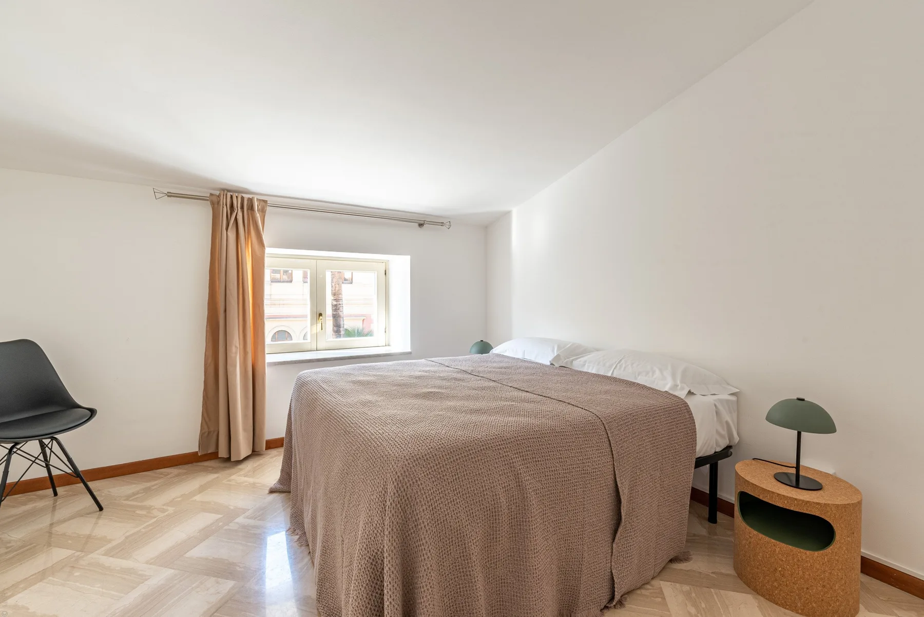 Un dormitorio luminoso con una cama, una ventana y una mesita de noche.