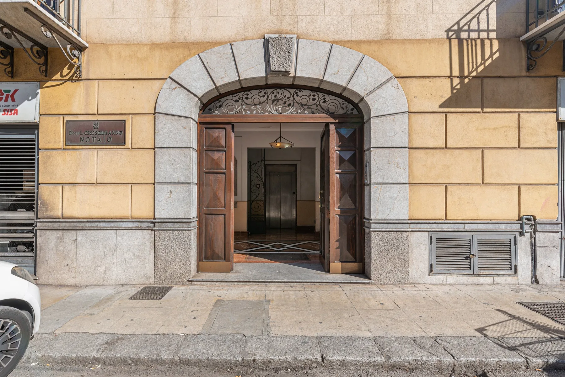 Entrada de edificio con arco de piedra, puertas de madera abiertas y suelo de baldosas en el interior.