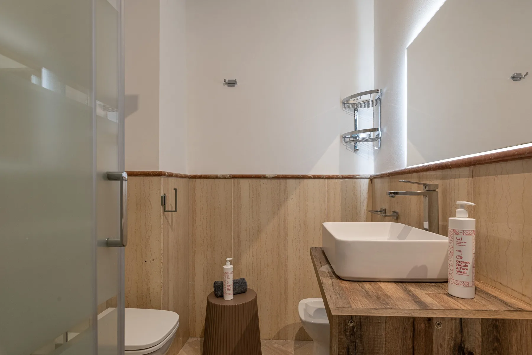 Un baño con ducha de vidrio, inodoro y lavabo sobre un tocador de madera.