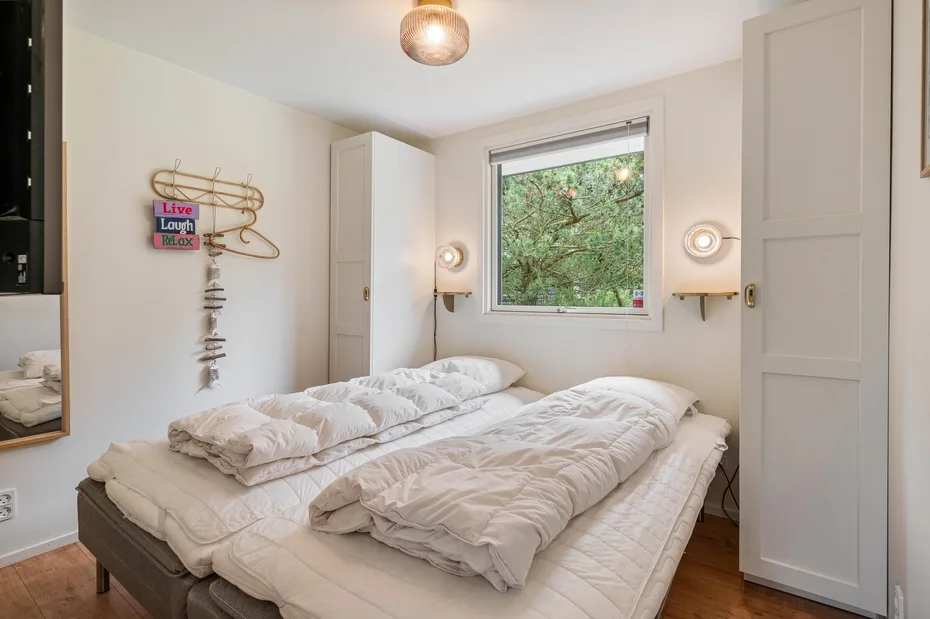 Un dormitorio con una cama bajo una ventana que da a árboles frondosos.