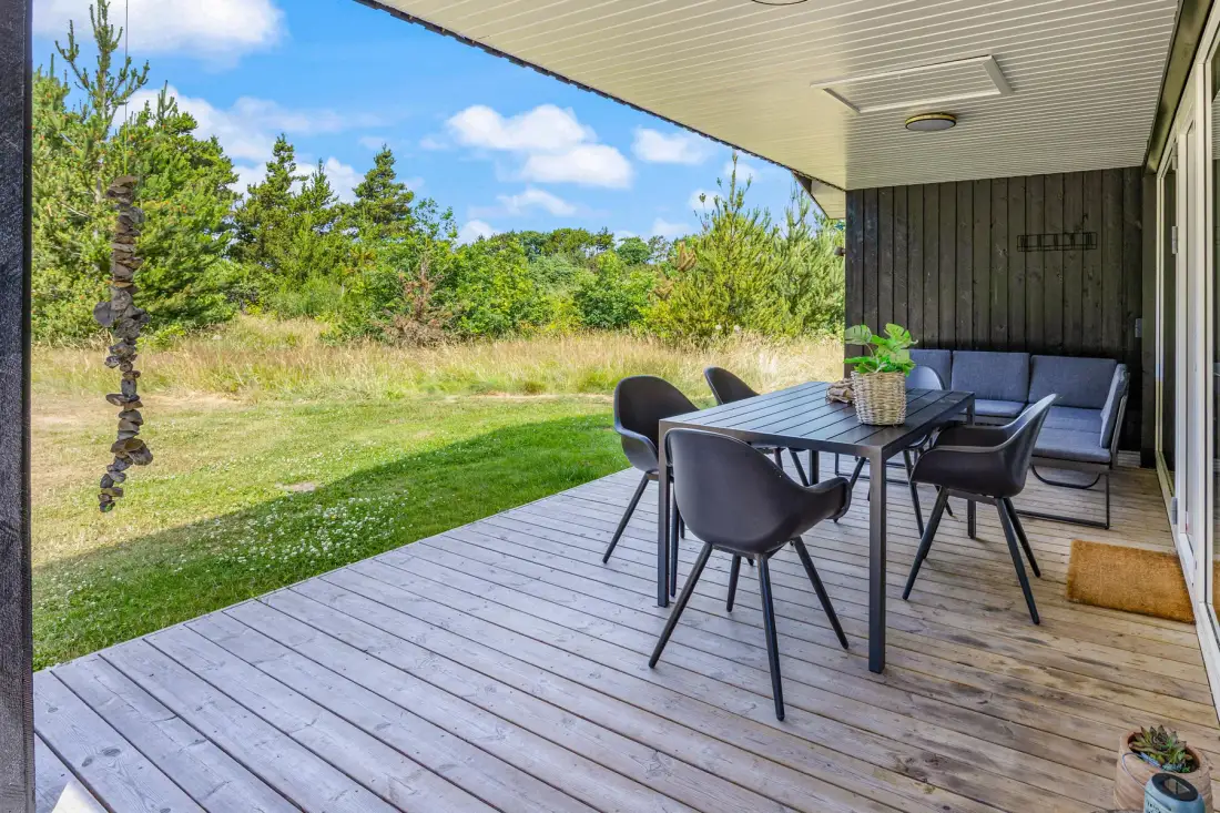 Una zona exterior cubierta con mesa de comedor da a un jardín con césped.