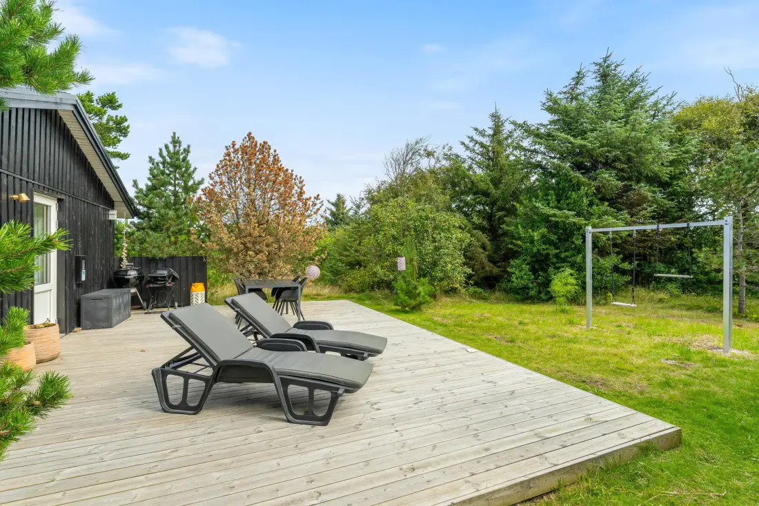 Una terraza de madera con asientos al aire libre y un jardín junto a una casa oscura.