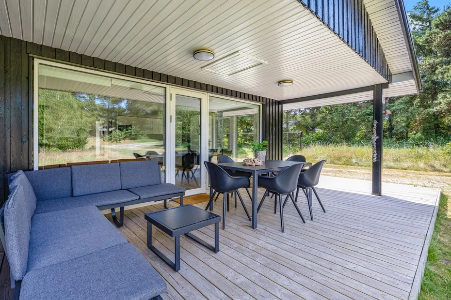 Zona de estar exterior cubierta con una mesa de comedor junto a grandes puertas de vidrio.