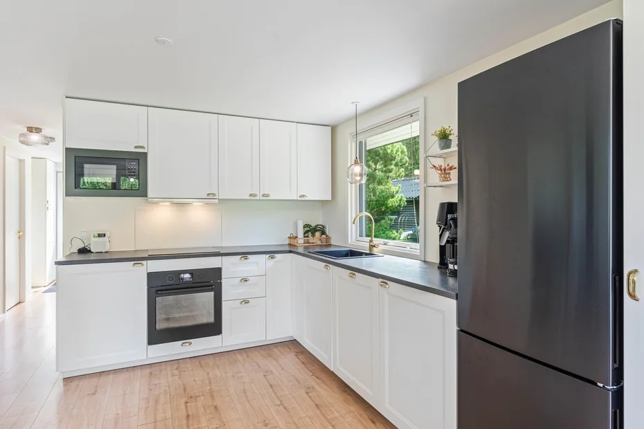 Una cocina luminosa con gabinetes blancos, encimeras oscuras y un refrigerador grande.