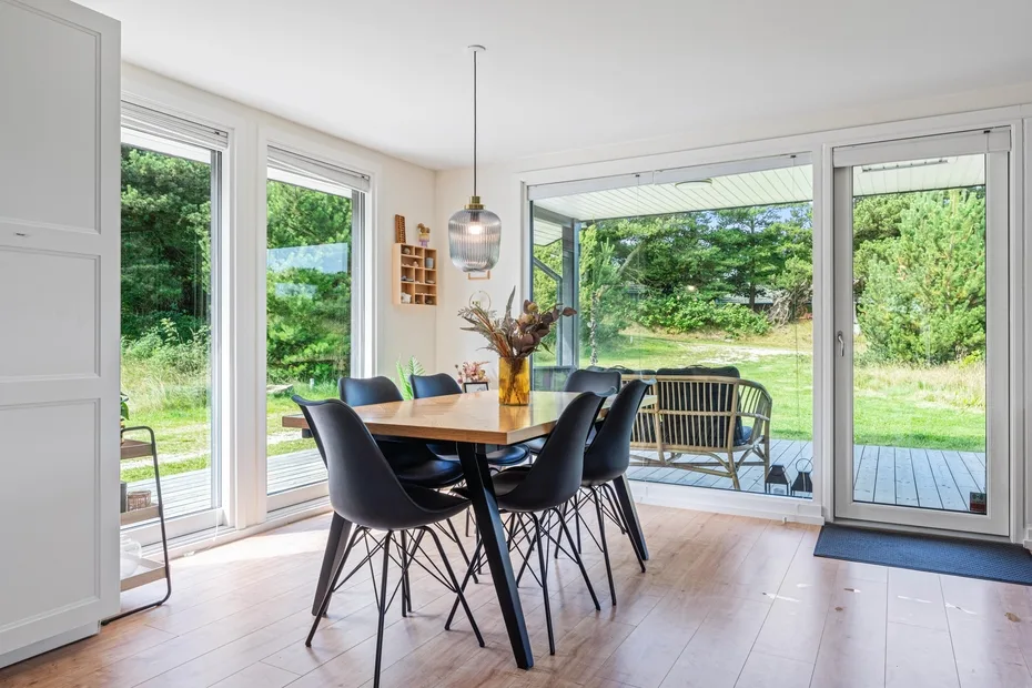 Comedor con una mesa de madera y asientos oscuros junto a grandes puertas de vidrio.