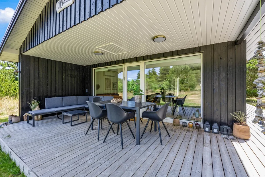 Comedor exterior cubierto con mesa y asientos junto a grandes ventanas.