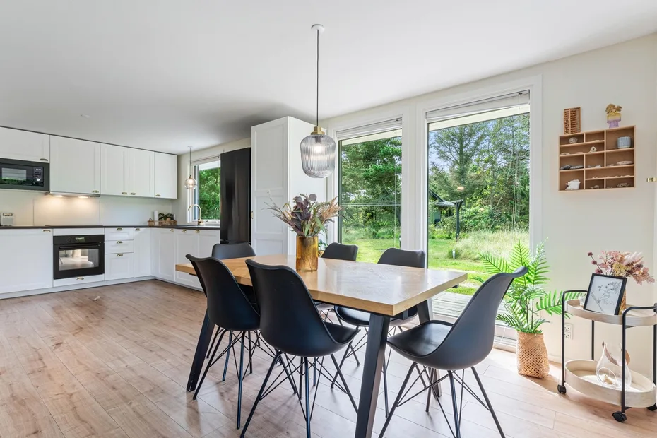 Un comedor luminoso con una mesa de madera junto a grandes ventanales que dan a la vegetación.