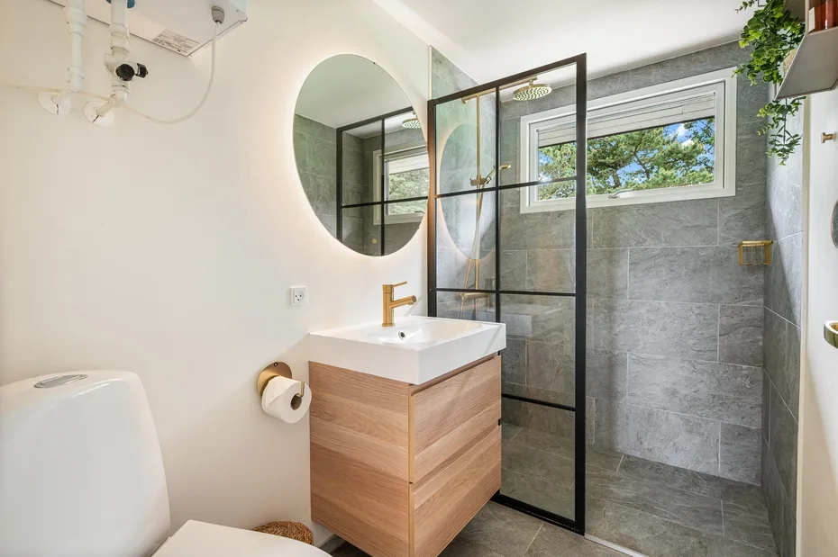 Un baño moderno con mueble de madera, espejo y ducha con mampara de vidrio.